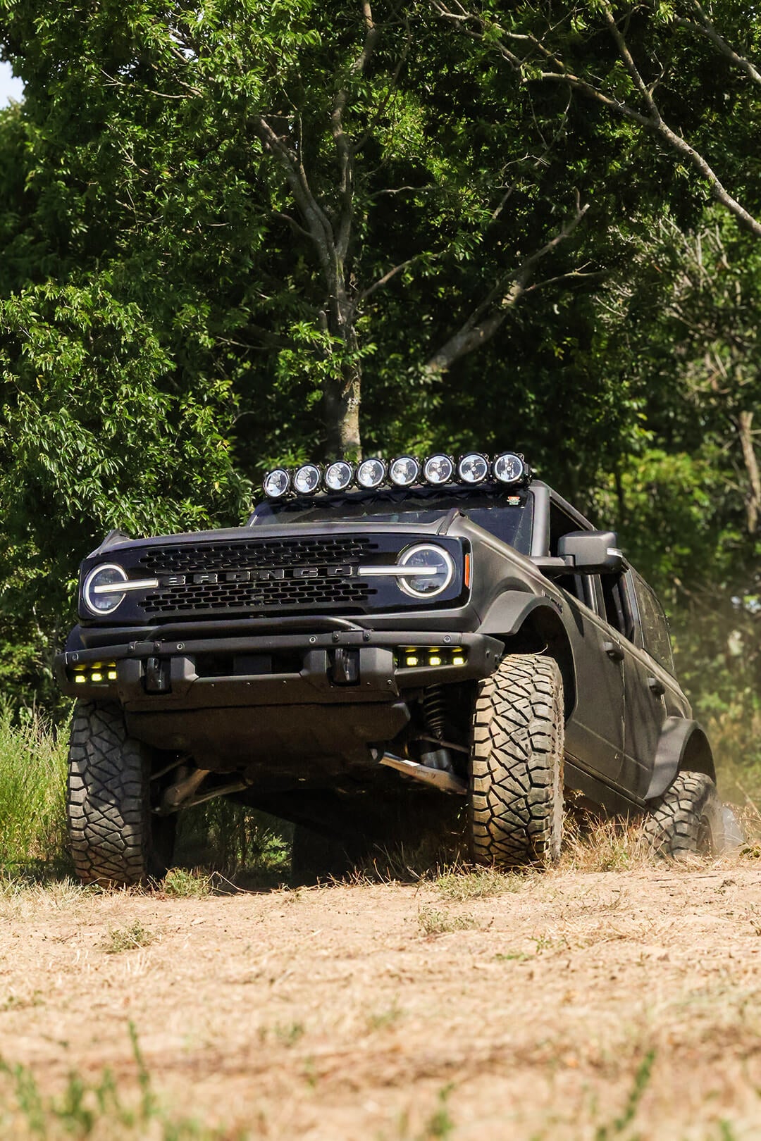 A front view of a black Ford Bronco with a roof light bar, off-roading.