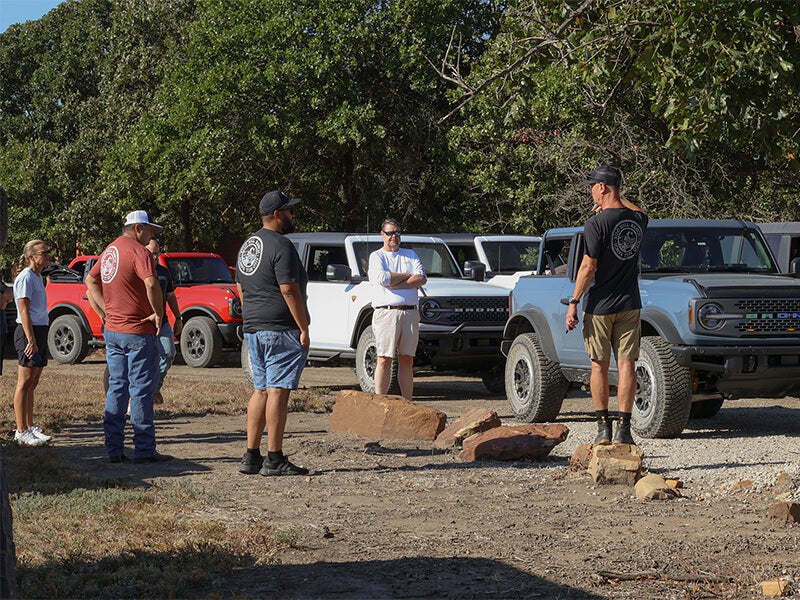 A group of people standing next to several Ford Broncos outdoors.