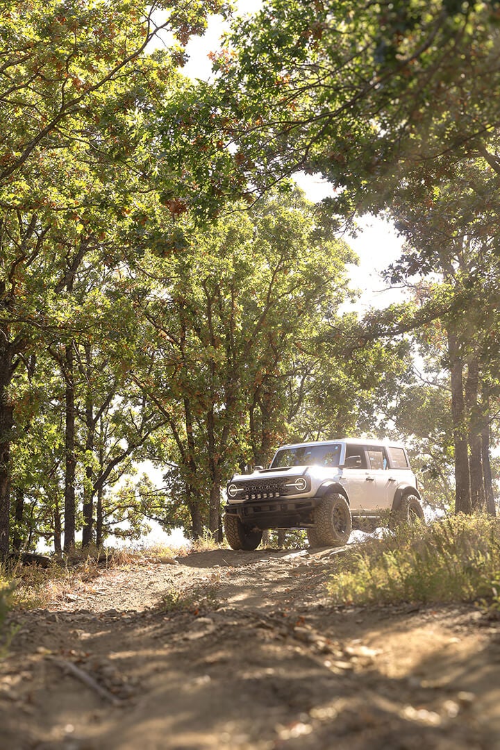 A white Ford Bronco driving on a dirt road.