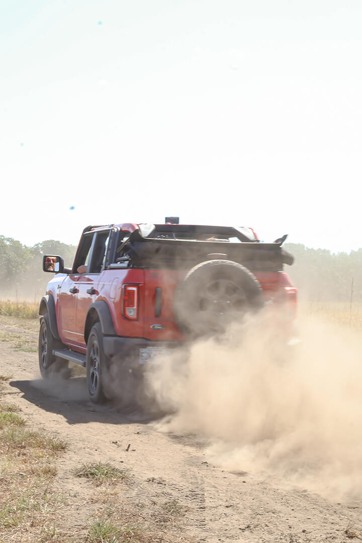 A red Ford Bronco kicking up dust on a dirt trail.