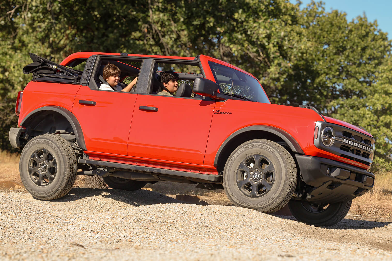 A side view of a red Ford Bronco driving on a dirt road.