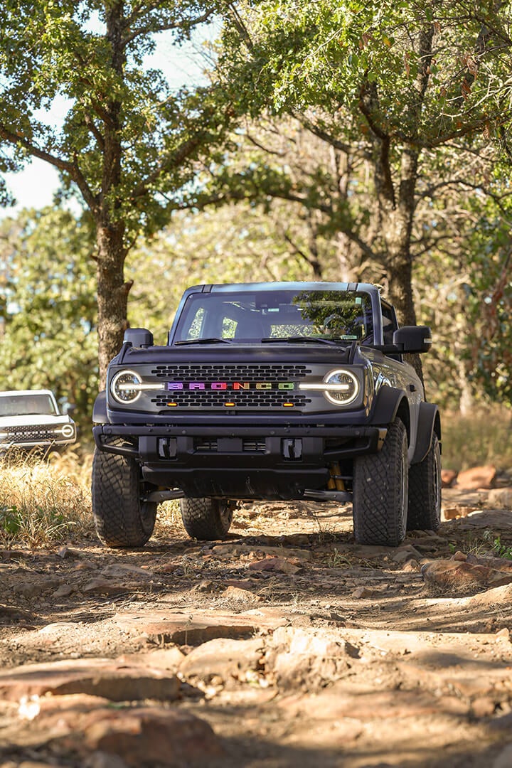 A front view of a white Ford Bronco with its lights on.
