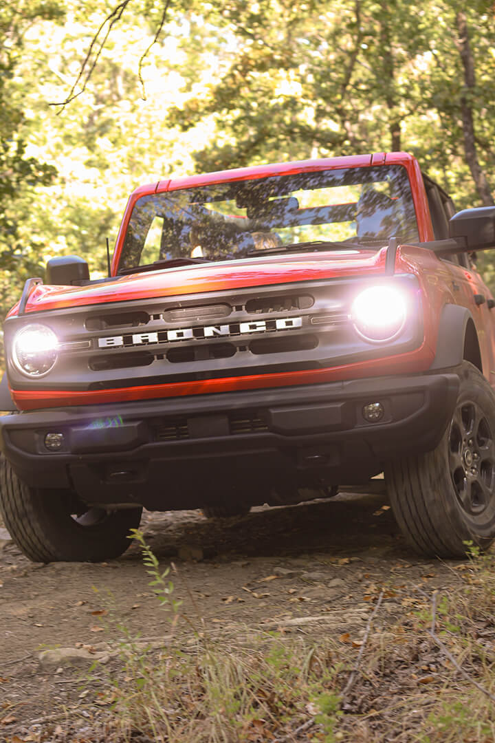 A front view of a red Ford Bronco with its lights on.