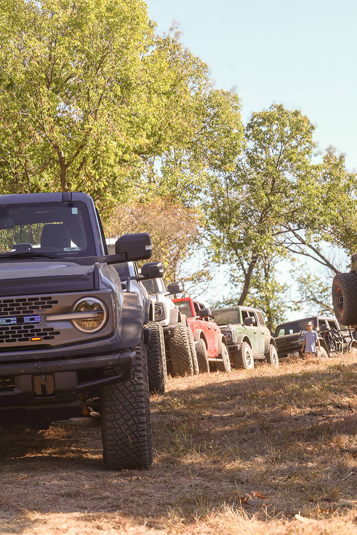 A line of Ford Broncos driving on a dirt road.
